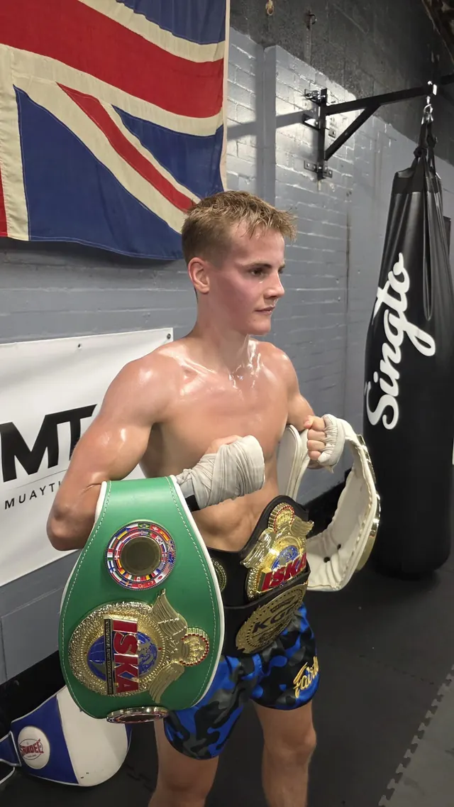 Pride Gym champion holding his title belts beside a heavy bag