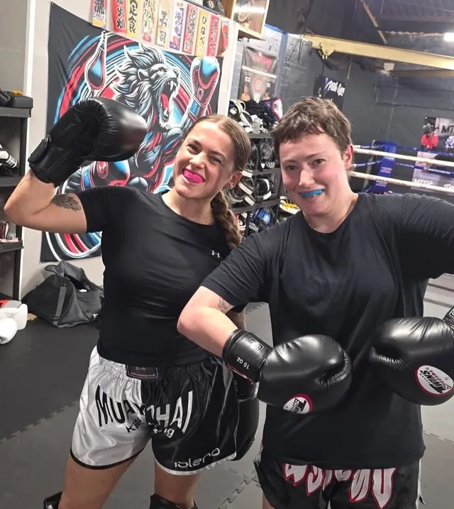 Two women smiling in gloves and gum shields after a Muay Thai training session at Pride Gym